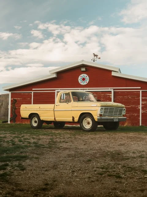 Classic cream Ford truck parked outside a red barn